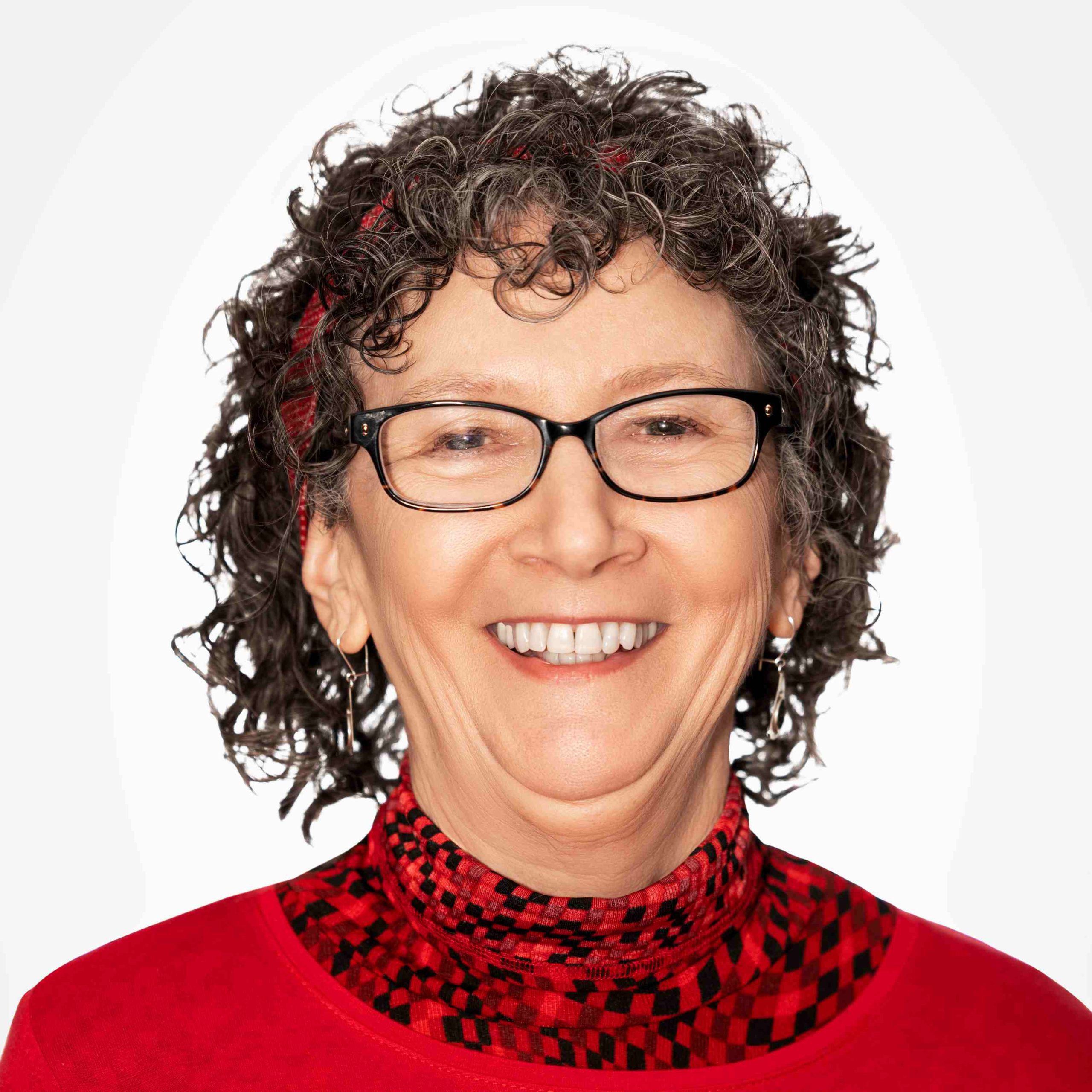 Terri Neff - female, with short dark curly hair wearing glasses and a red sweater and turtleneck