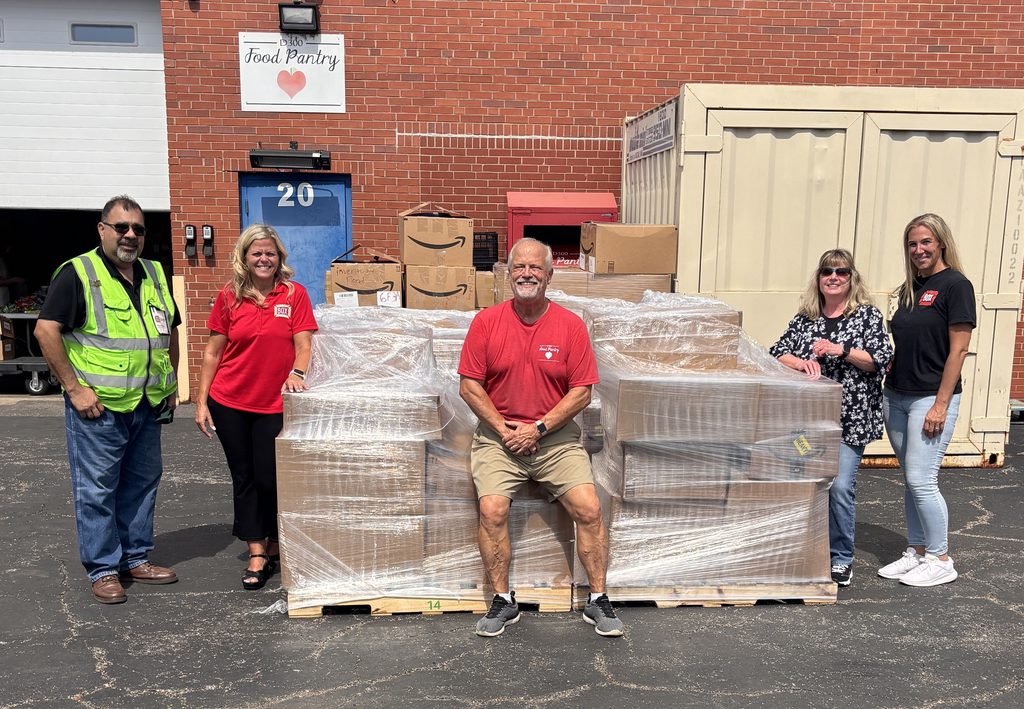 Five people - two men and three women - standing in front of the D300 Food Pantry, and a huge number of boxes on wood pallets.