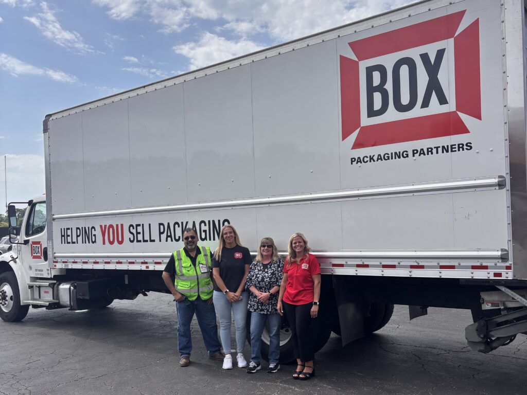 Four people standing in front of a semi truck with the logo for Box Packaging.